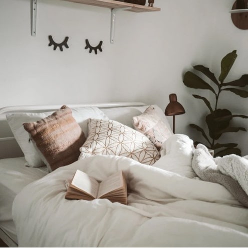 Cozy bedroom with neutral bedding, decorative pillows, and indoor plants for a calming atmosphere.