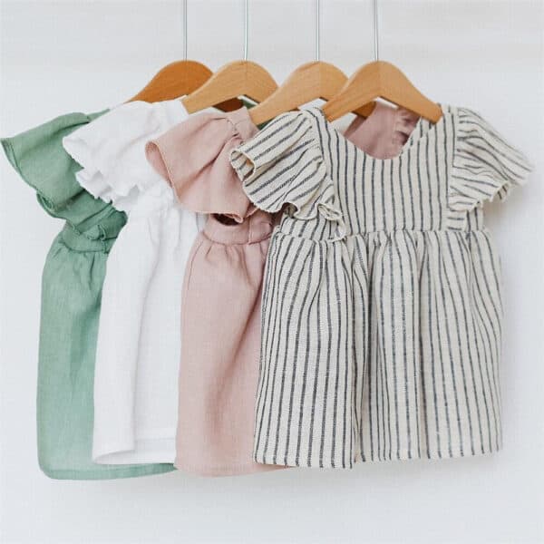 Soft pastel-colored baby dresses hanging on wooden hangers, ideal for nurturing and stylish infant c.