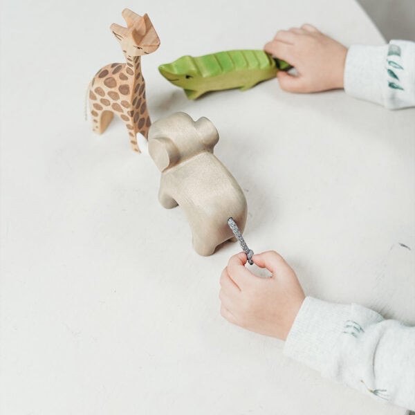 Wooden animal toys and a child's hand playing with a green crocodile figure on a white surface.