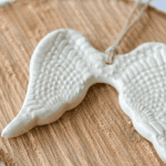 White ceramic angel wing ornament on wooden surface, symbolizing purity and protection.