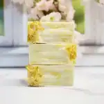 Gentle soap bars with natural ingredients on a white surface, with a blurred floral background.