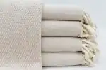 Soft beige woven and knitted blankets stacked, showcasing cozy, high-quality textiles for home comfo.