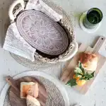Handmade soap with floral design in a woven basket, natural setting with bread and green drink.