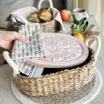 Hand lifting a decorative pink ceramic plate from a woven basket.