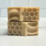 Cream-colored handmade soap bars with textured patterns, stacked on a white surface.