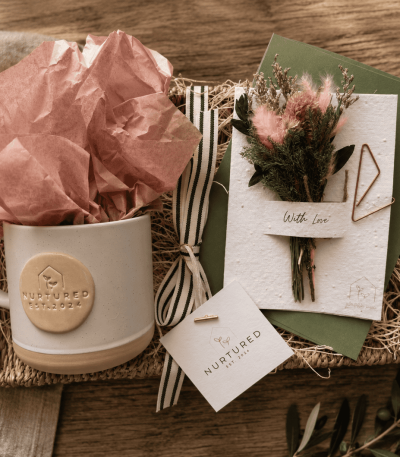 Thoughtful morning gift bundle featuring a linen Nurtured signature ceramic mug, plantable wildflower greeting card with dried floral bouquet, and woven seagrass decorative tray styled for cozy mornings and elevated gifting.