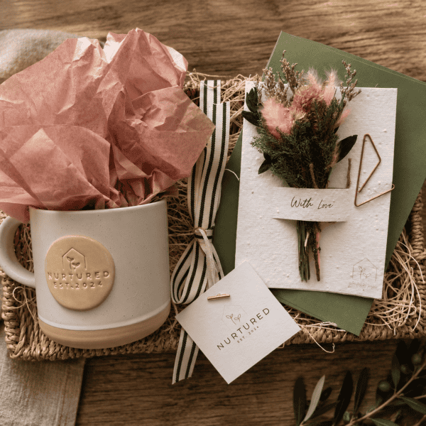 Thoughtful morning gift bundle featuring a linen Nurtured signature ceramic mug, plantable wildflower greeting card with dried floral bouquet, and woven seagrass decorative tray styled for cozy mornings and elevated gifting.