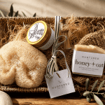 Luxury self-care gift bundle featuring a lavender vanilla soy candle, honey oat artisan soap bar, natural loofah sponge, jute soap saver pouch, decorative glass match vial, and woven seagrass tray styled for calming home rituals and elevated gifting.