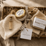 Luxury self-care gift bundle featuring a seagrass woven tray, eucalyptus spearmint soy candle, artisan honey oat soap bar, sisal exfoliating spa mitt, natural soap saver pouch, and decorative glass matchstick vial styled for elevated home gifting and relaxation rituals.