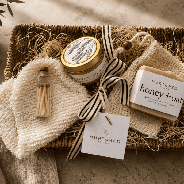 Luxury self-care gift bundle featuring a seagrass woven tray, eucalyptus spearmint soy candle, artisan honey oat soap bar, sisal exfoliating spa mitt, natural soap saver pouch, and decorative glass matchstick vial styled for elevated home gifting and relaxation rituals.
