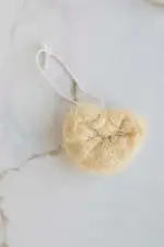 Soft natural loofah sponge for skincare and exfoliation, hanging on a white marble surface.