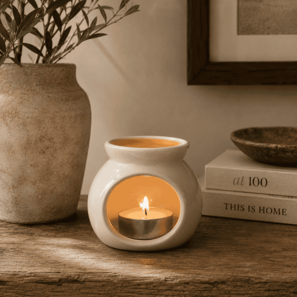 White ceramic petite wax melter with glowing tealight candle styled on a rustic wooden surface with warm neutral décor and soft ambient lighting.