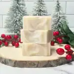Creamy handmade soap bars on a wooden slice with festive red berries and snow-covered pine trees in.