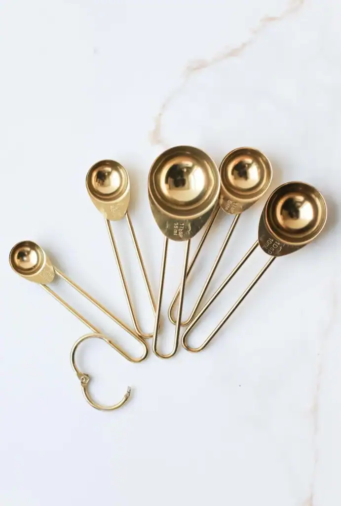 Stainless steel (gold finished) measuring spoons set on white marble background, kitchen utensils, cooking tools, culinary acce.
