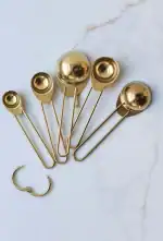 Set of gold safety pins and a small gold hoop earring on white marble background.