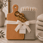 Luxury kitchen gift set featuring a Canadian maple cutting board, organic Turkish hand towel, and stainless steel measuring spoons styled in a warm neutral inspired setting.