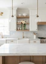 Elegant white kitchen with open shelving, marble countertops, and gold accents, showcasing modern an.