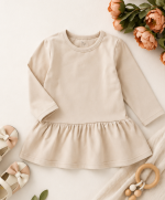 Organic cotton long sleeve baby dress with gathered skirt in a soft neutral cream color.